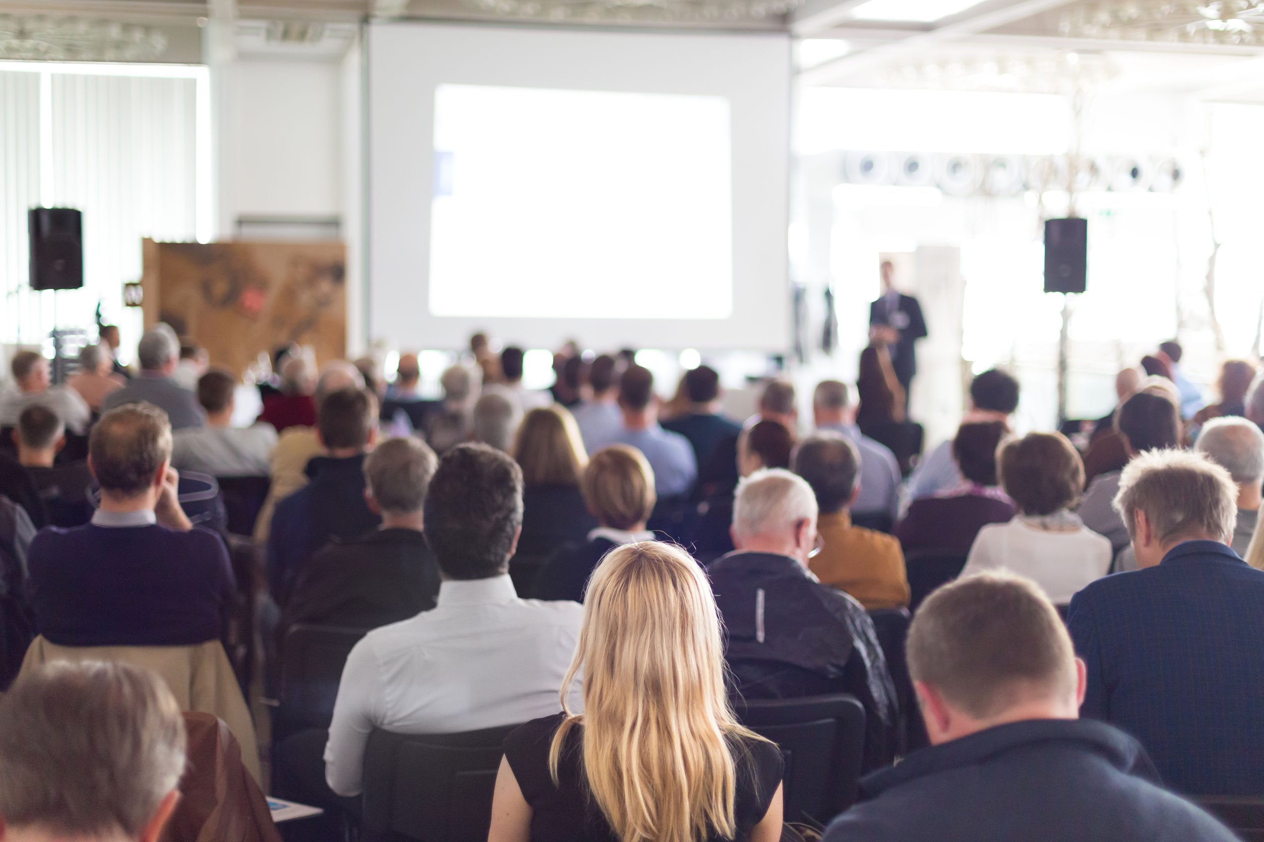 A group of people at an event, watching a presentation.