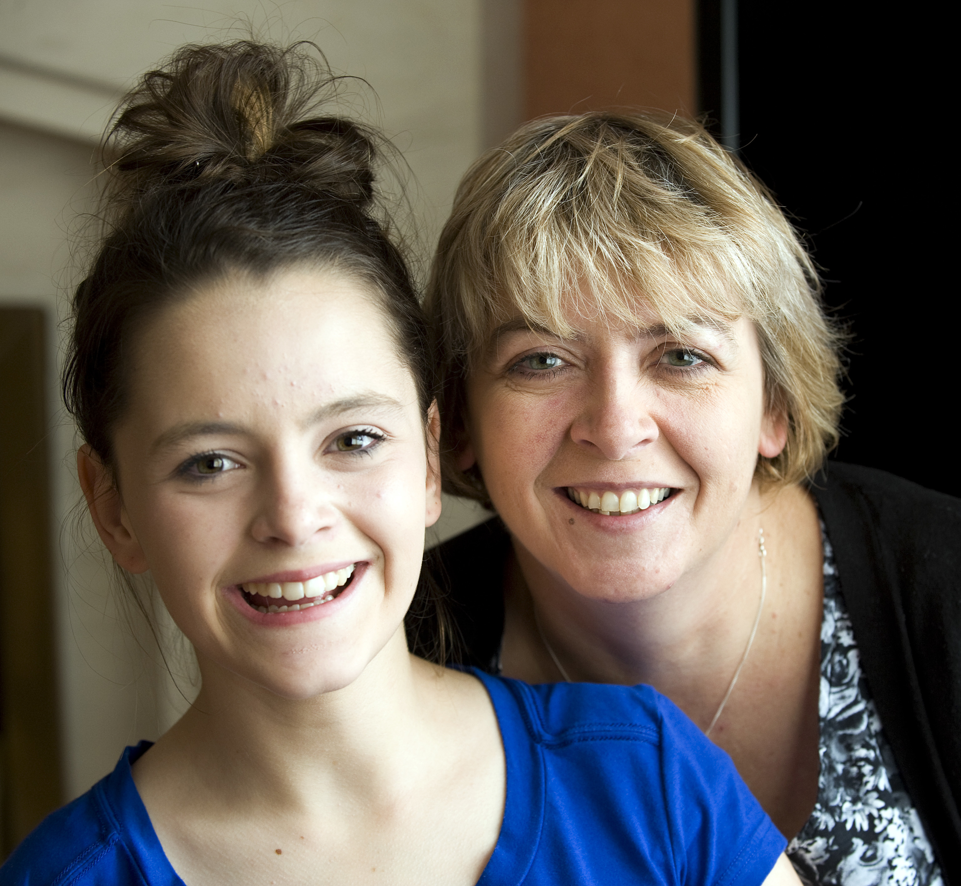 A woman and a young girl smiling and looking towards the camera.