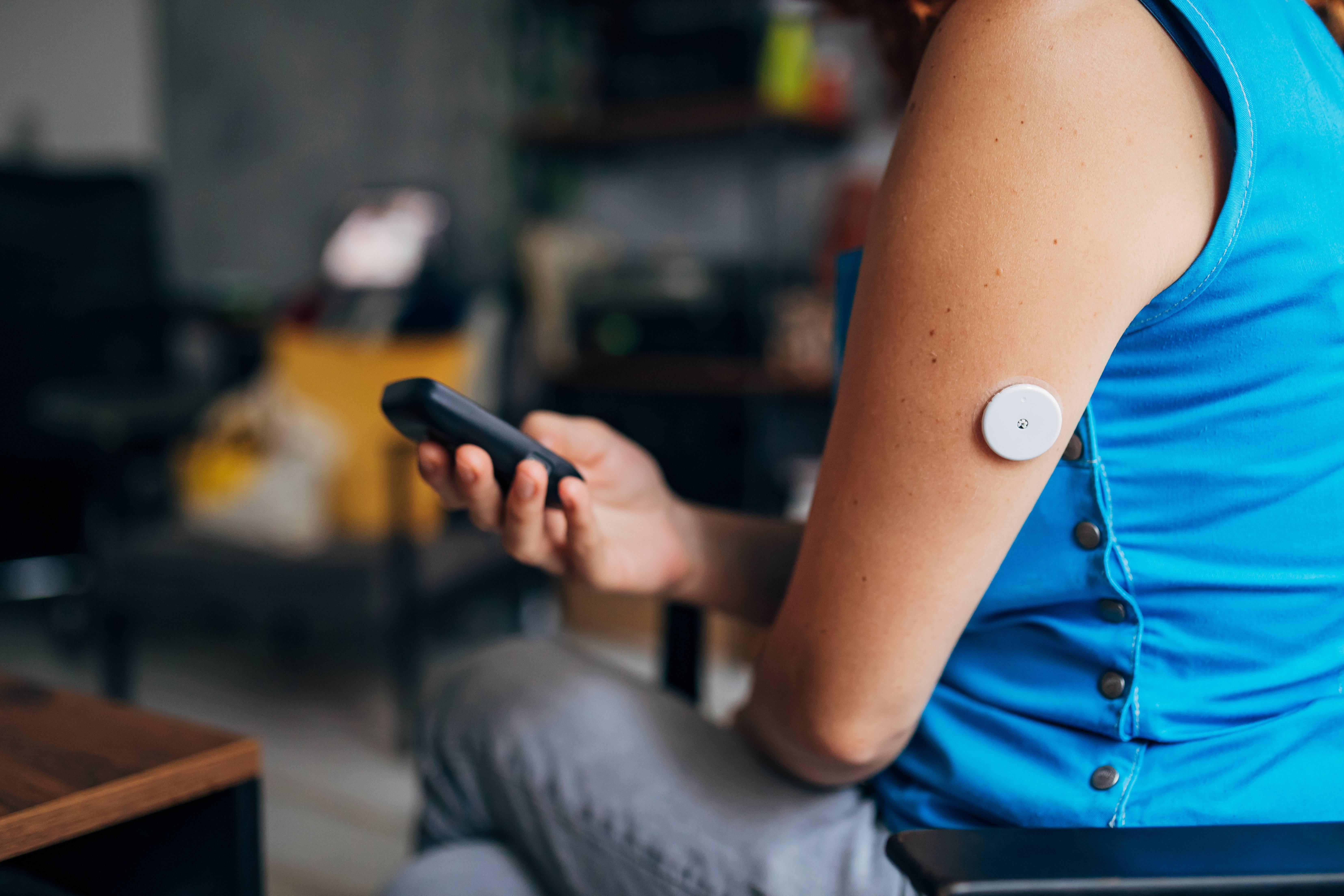 A woman using a diabetes glucose monitor attached to the back of her arm.