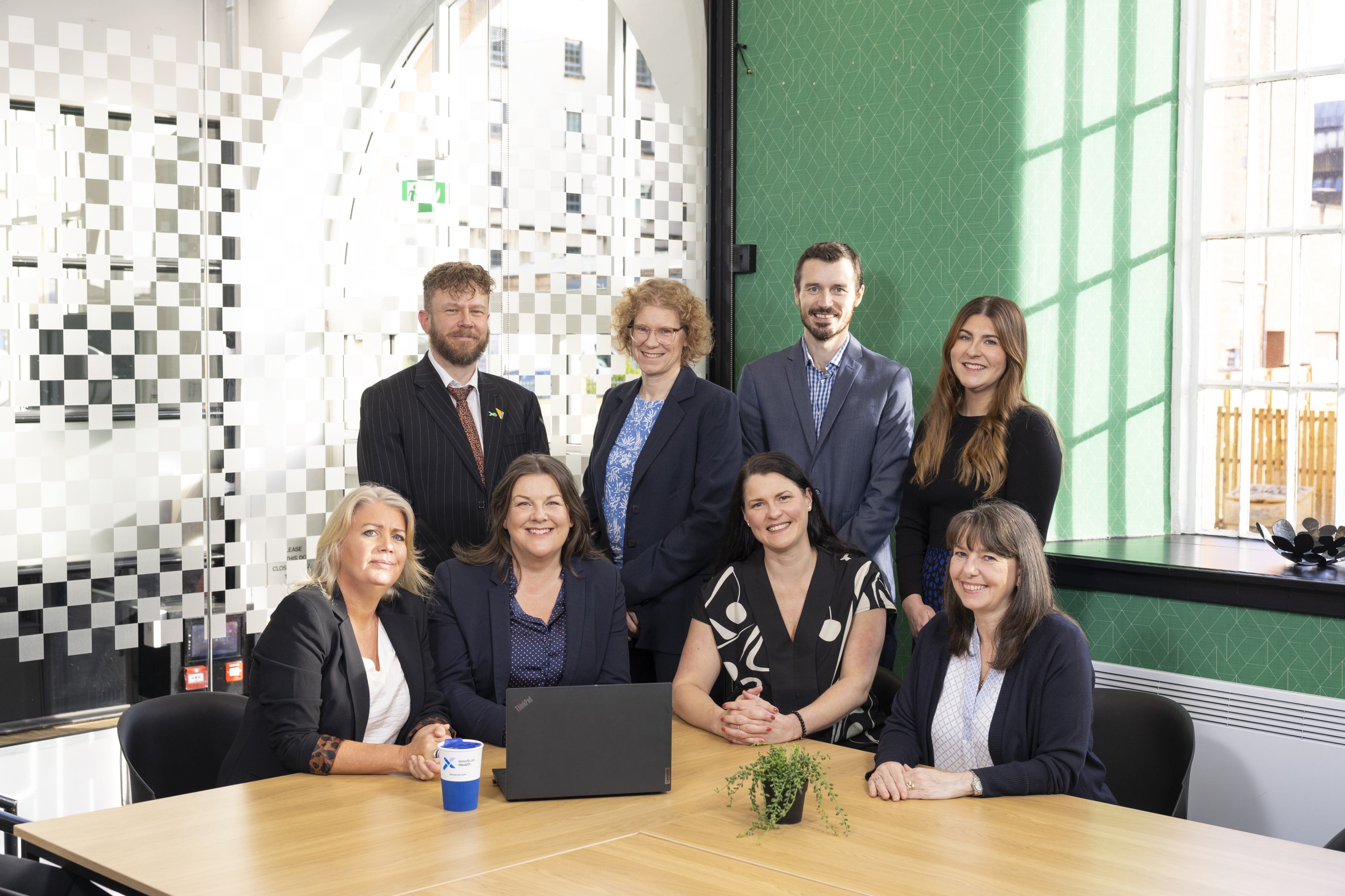 A group of InnoScot Health staff seated around an office table, smiling to the camera.