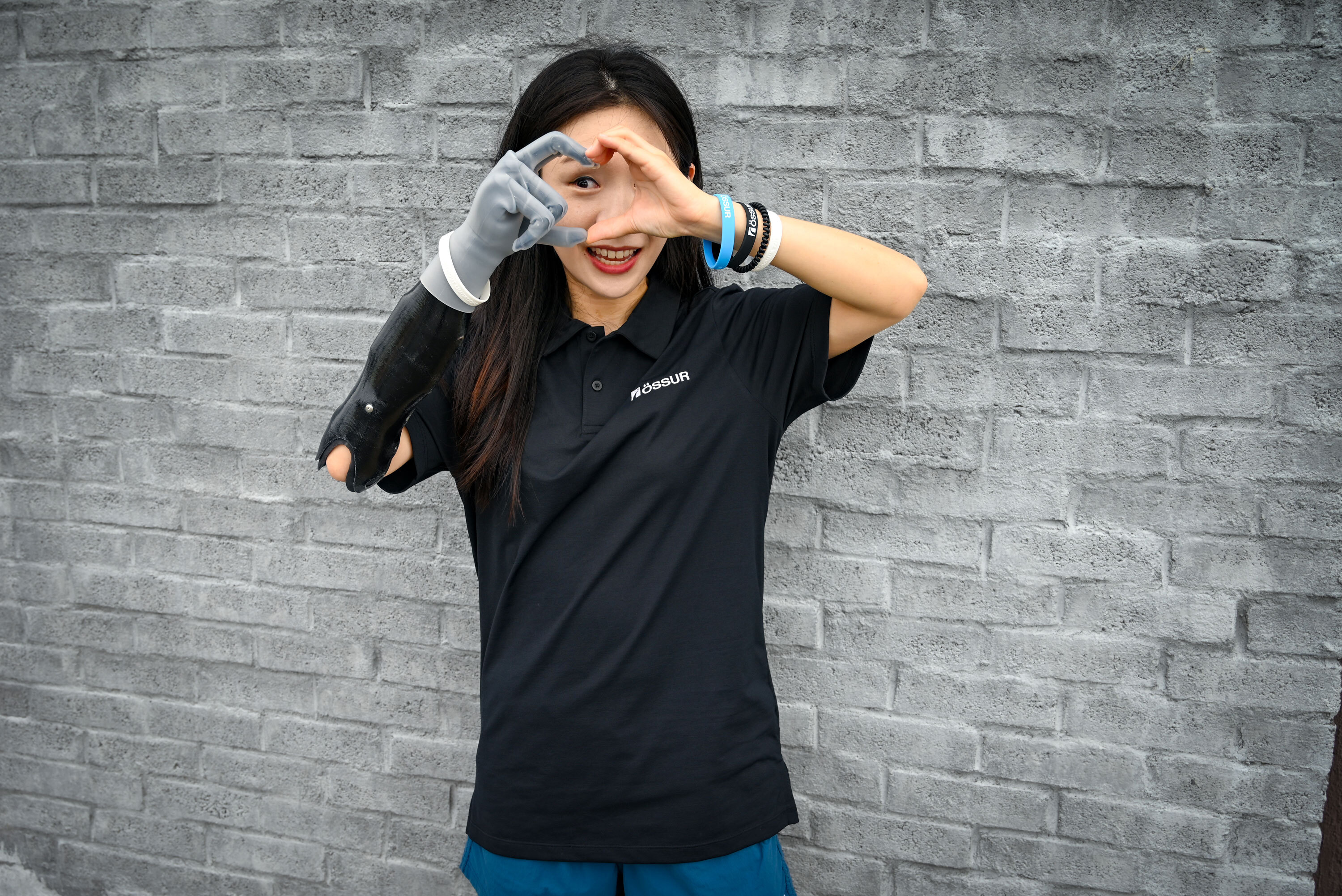 A woman making a heart shape with her hands, one of which is a Touch i-Limb.