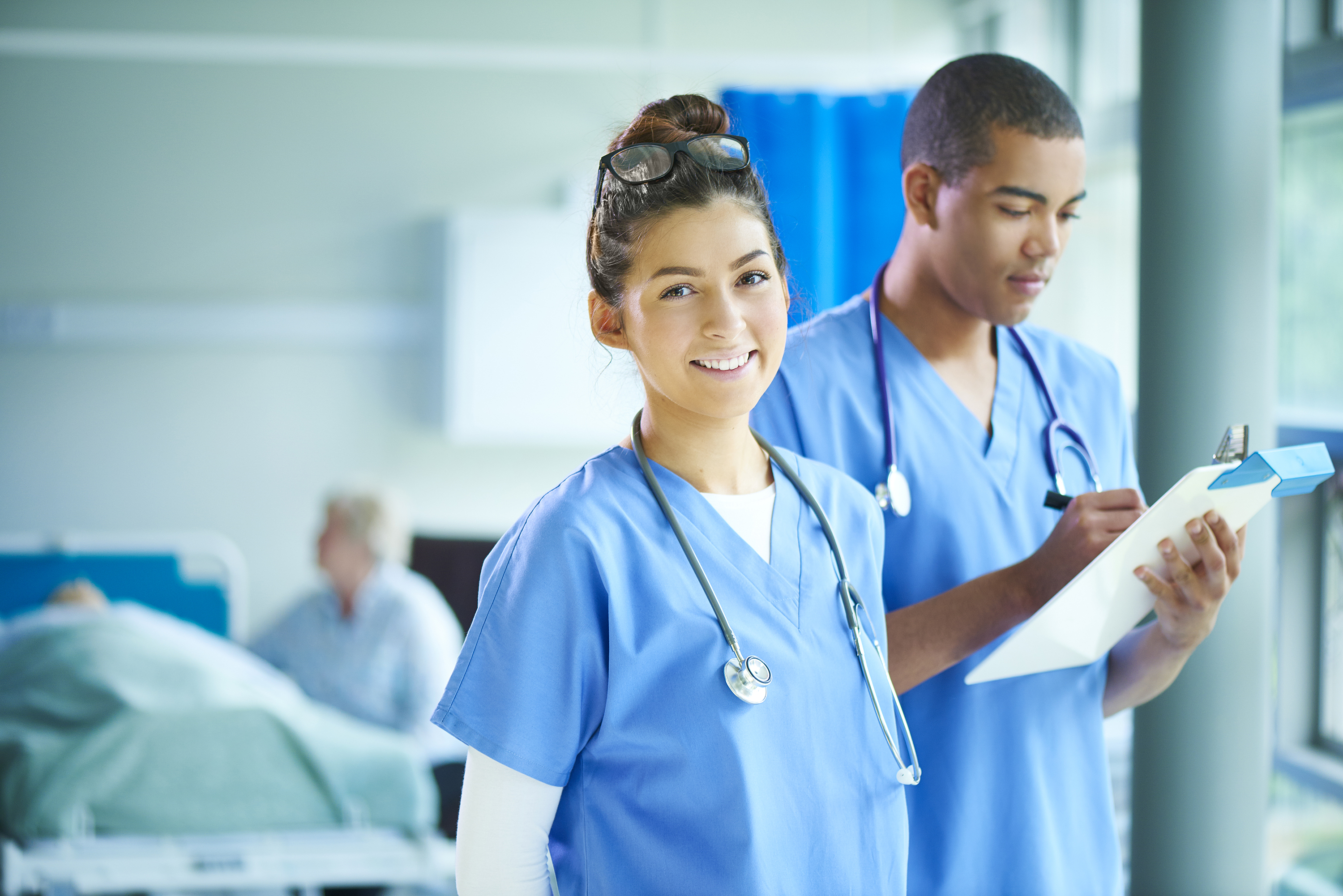 Two healthcare professionals on a ward, one of them looking towards the camera and smiling.