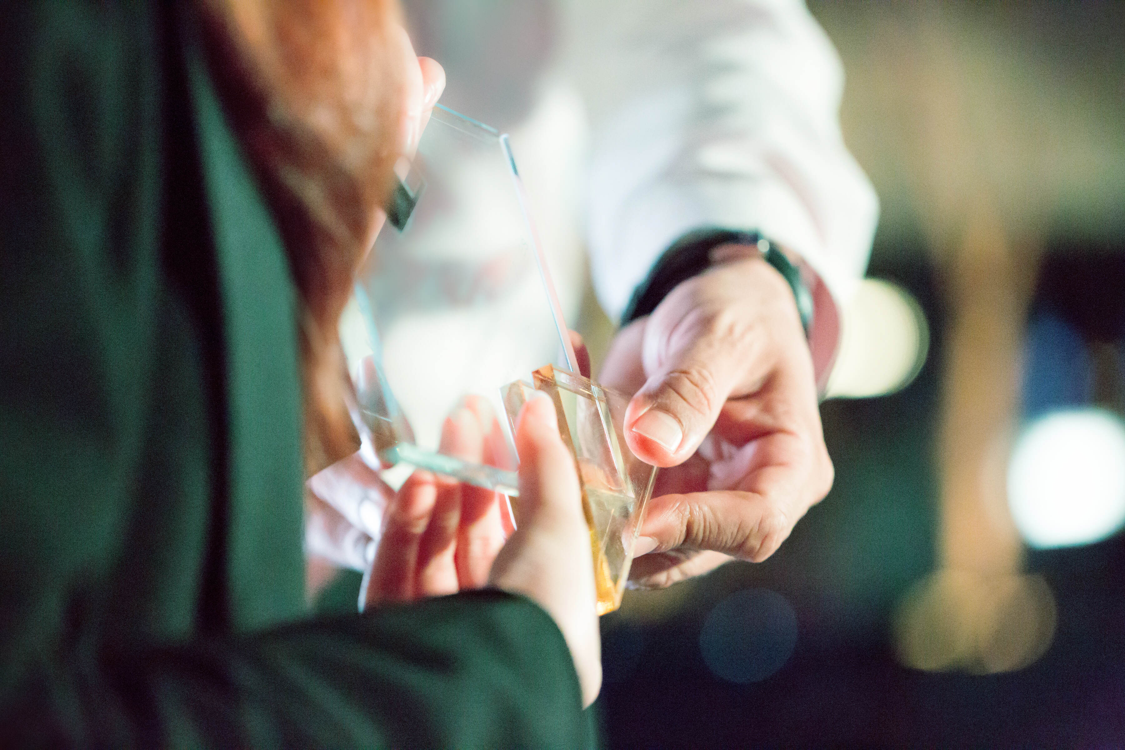 A man being presented with an award. Only the glass award, two sets of hands, a white shirt and a green blazer are visible.