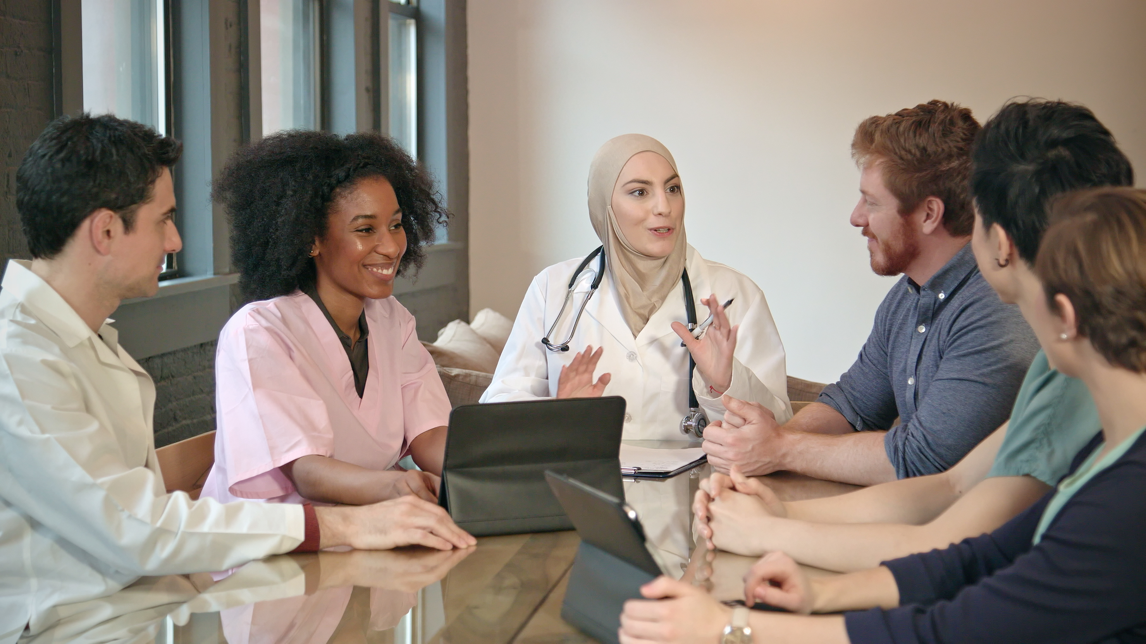 A confident muslim woman doctor meets with other healthcare professionals and entrepreneurs around a table in an office setting.